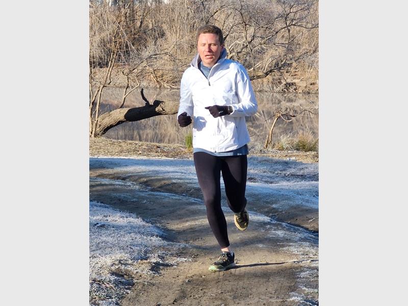A man in a white jacket and black pants is running on a trail.