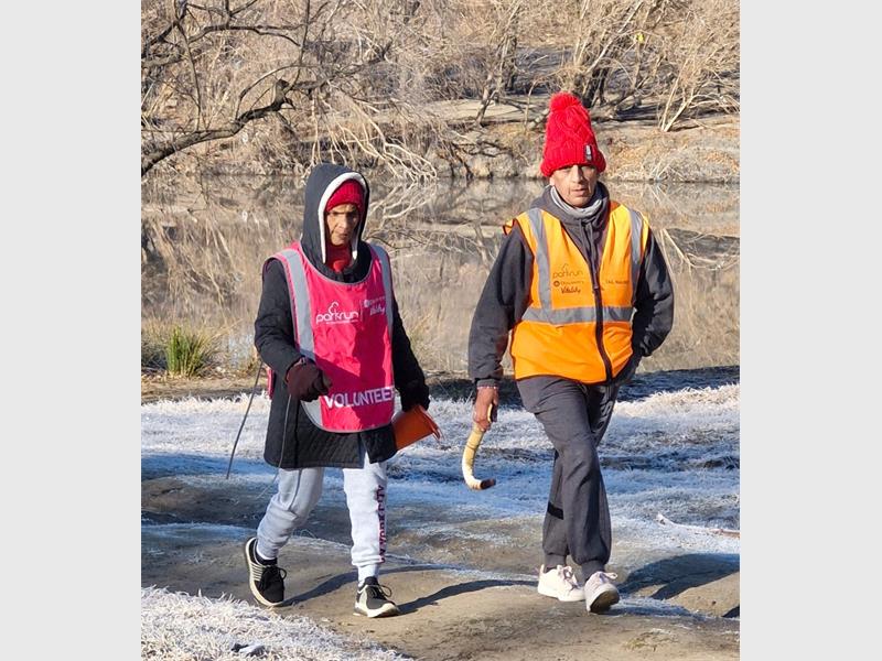 Two people wearing orange vests and red hats walking along a path.