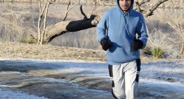 A man in a blue hoodie running on a snowy path.