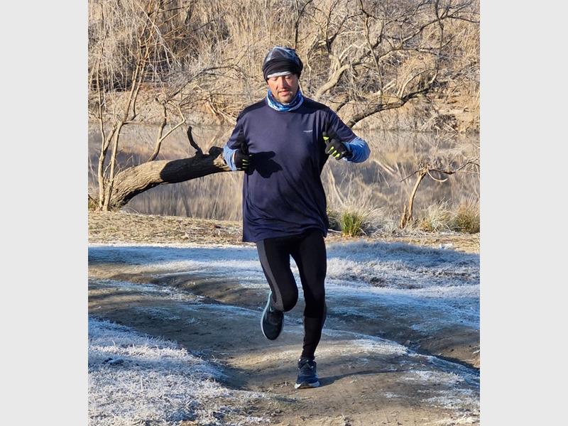 A man in a blue shirt and black hat running on a path.