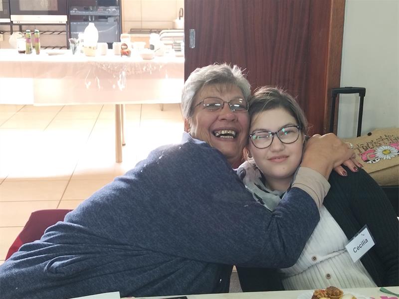 A woman and a girl hugging at a table with food.