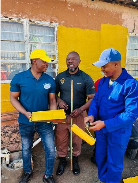 Three men in blue and yellow work clothes holding boxes.