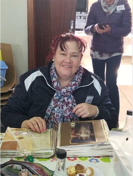 A woman sitting at a table with a book and a plate of food.