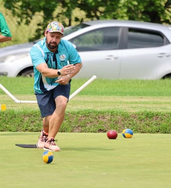 A man in a blue shirt playing a game of lawn bowls.