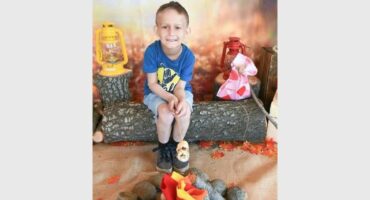 A boy sitting on a log with a fire pit.