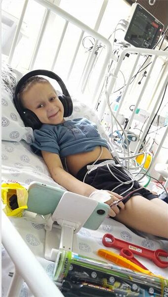 A young boy laying in a hospital bed with headphones on.