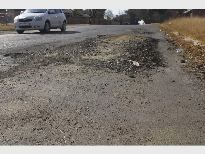 A car is driving down a road with a pothole in the middle.