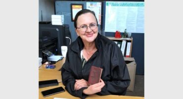 A woman in glasses holding a book in front of her.