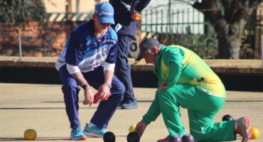 Two men playing bowls on a field with a ball.