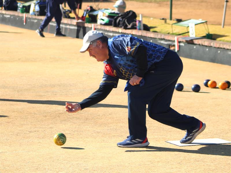 A man in blue shirt and black pants playing bowling.