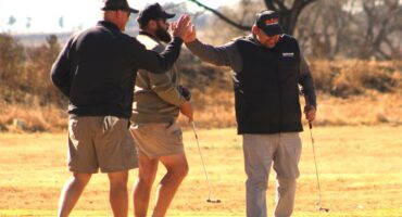 Three men are giving high fives on a golf course.