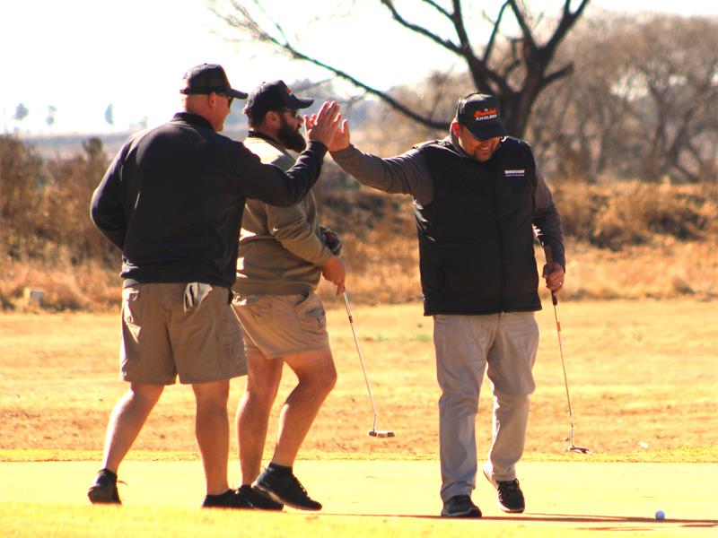 Three men are giving high fives on a golf course.