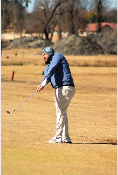 A man in blue jacket and white pants is playing golf.