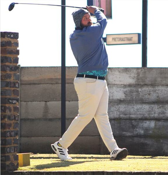 A man in a black shirt and khaki pants is swinging a golf club.