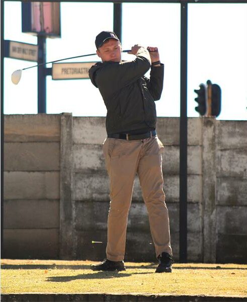 A man in a black shirt and khaki pants is swinging a golf club.