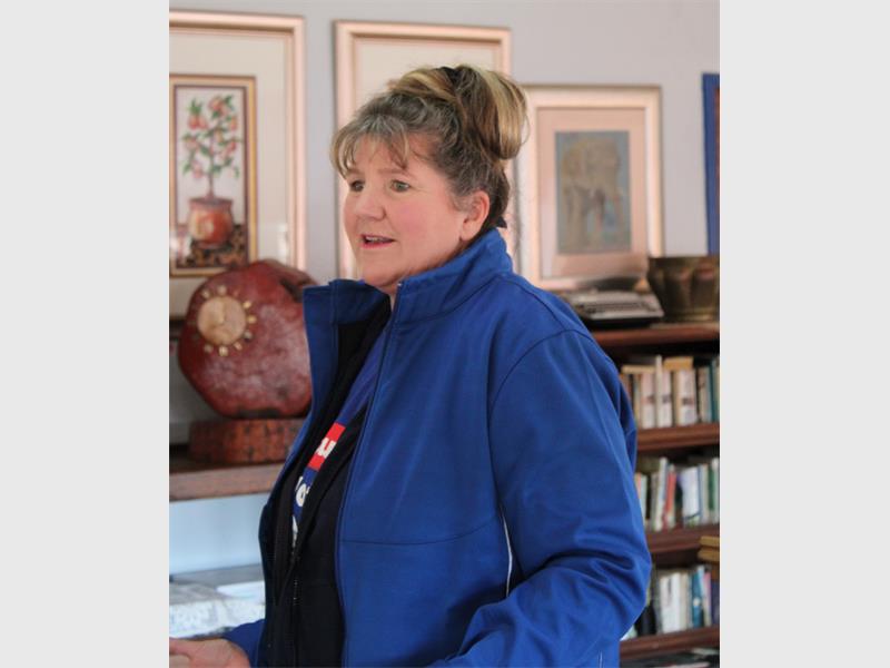 A woman in a blue jacket standing in front of a bookshelf.