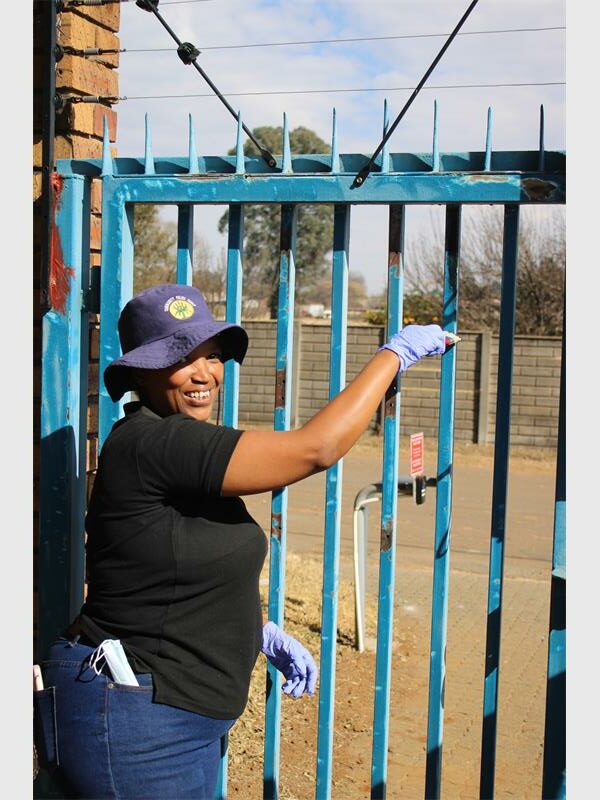 A woman wearing gloves and a hat is standing next to a gate.
