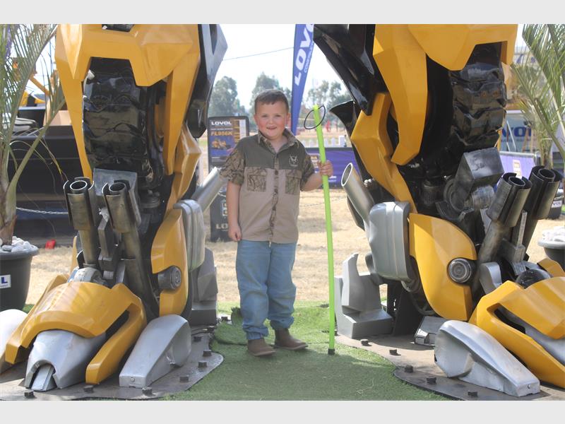 A young boy standing next to a giant robot.