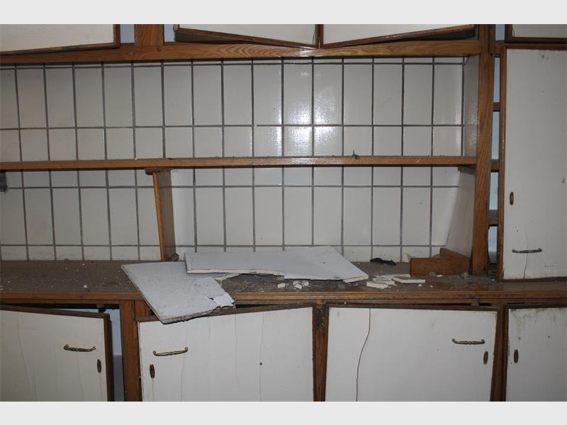A kitchen with broken cabinets and a broken counter.