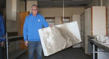 A man holding a large piece of white board in a room.