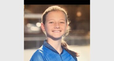 A young girl in a blue jersey smiling.