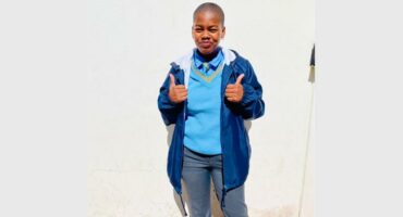 A young boy in blue jacket and jeans giving the thumbs up.