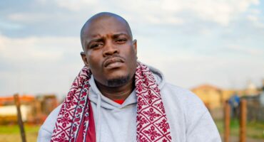 A man wearing a scarf and hoodie standing in front of a field.