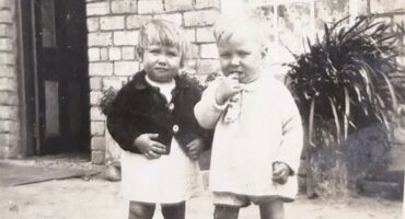 Two young children standing outside of a house.
