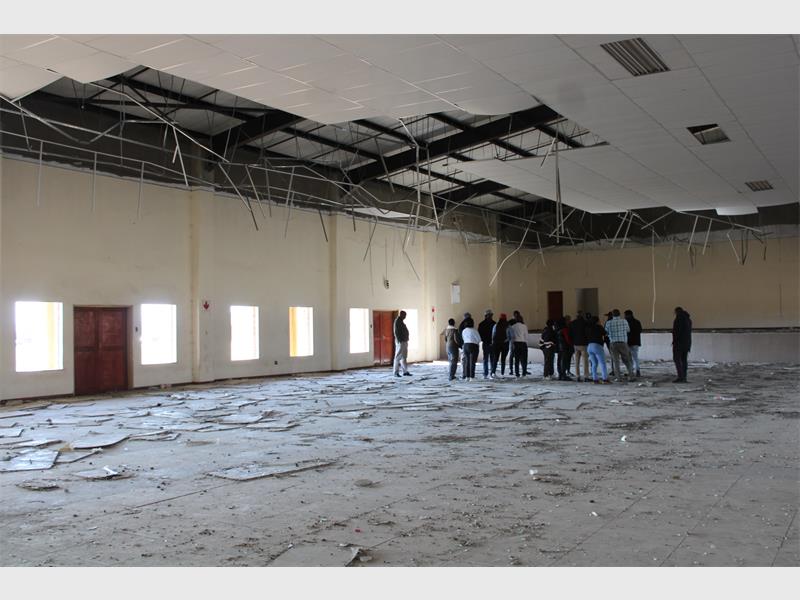 People standing in an empty room with broken windows.