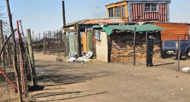 A shack with a fence and a car parked in front.