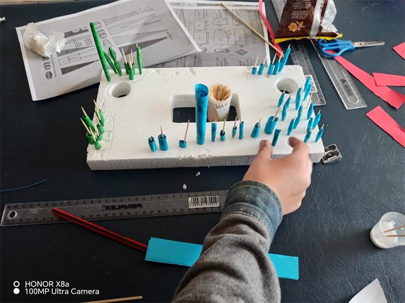 A person is making a model of a house with blue and green sticks.