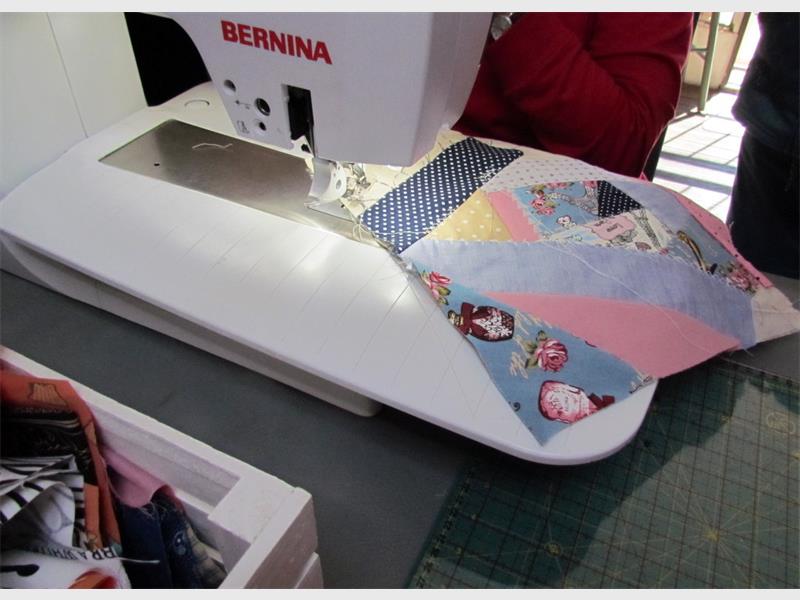 A sewing machine is cutting fabric on a table.