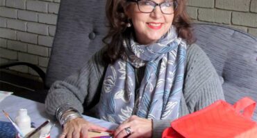 A woman with glasses and a scarf sitting at a table with a red bag.