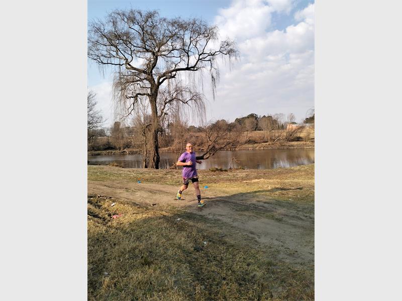 A man running in the grass near a river.