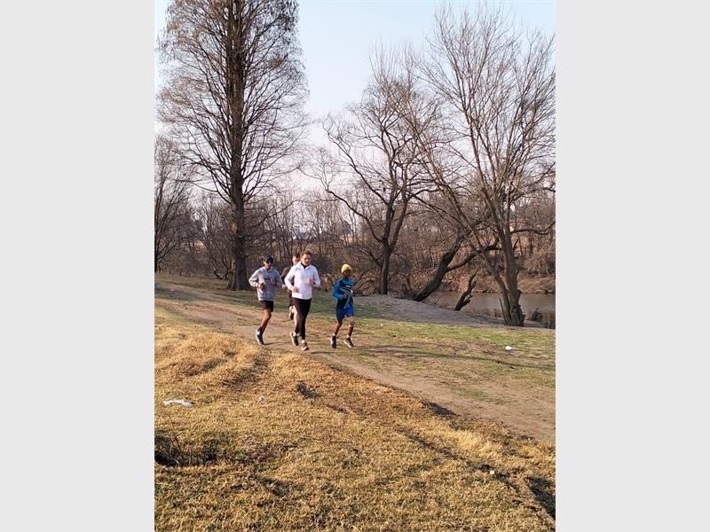 Three people running on a path near a river.