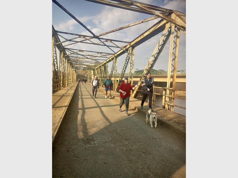 People walking on a bridge with a dog.