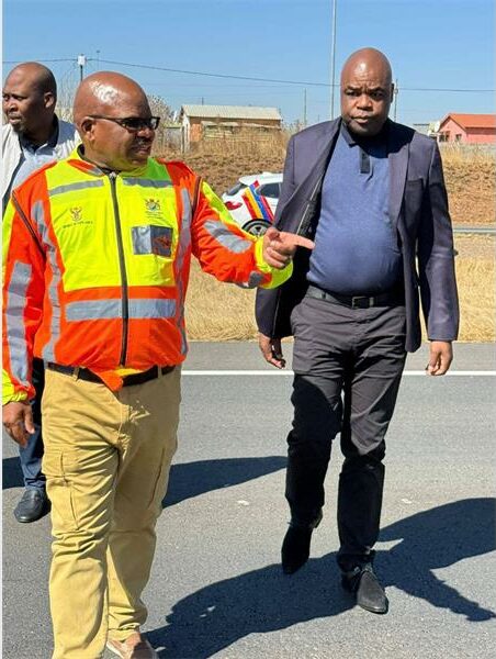 Two men in safety vests walking on the road.
