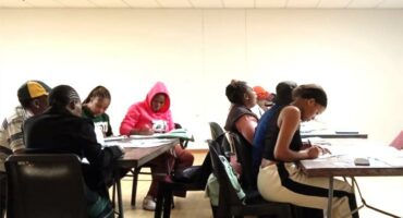 A group of people sitting at tables in a classroom.