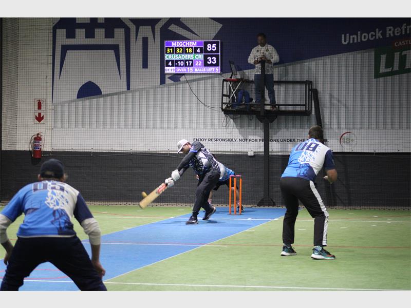A group of men playing cricket on an indoor court.