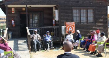 A group of people sitting outside a small house.