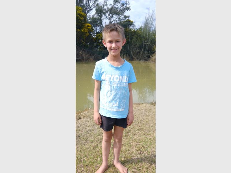 A young boy standing in front of a pond.