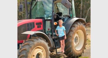 A young girl standing next to a tractor.