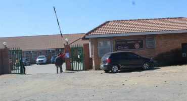 A man standing outside of a building with a car parked in front.