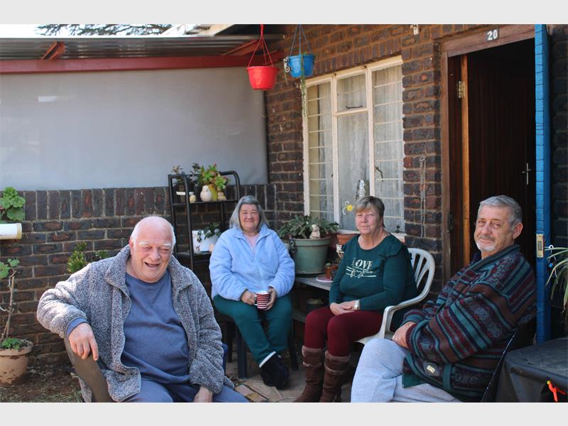 Four people sitting on a patio outside of a house.