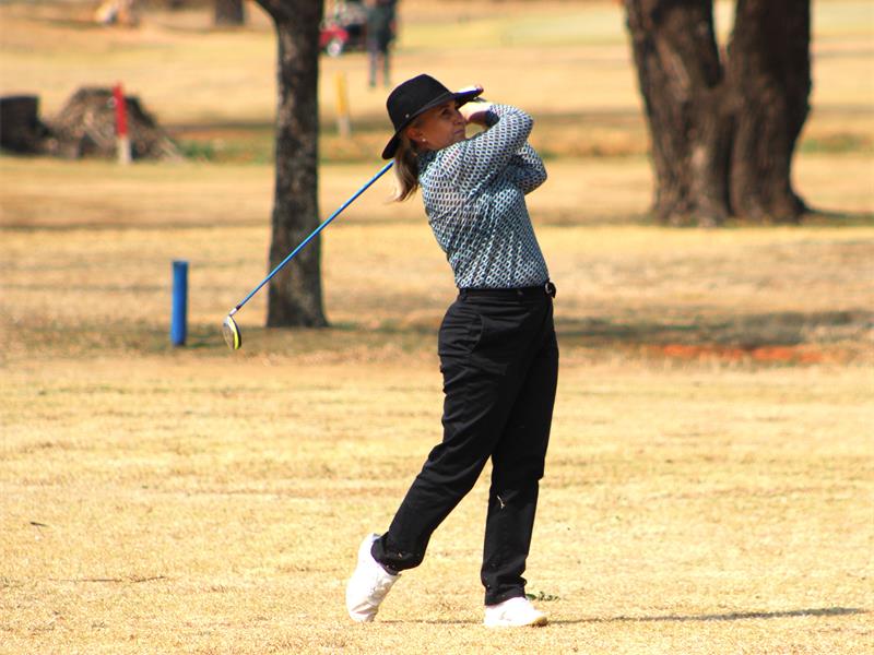 A woman swinging a golf club on a field.