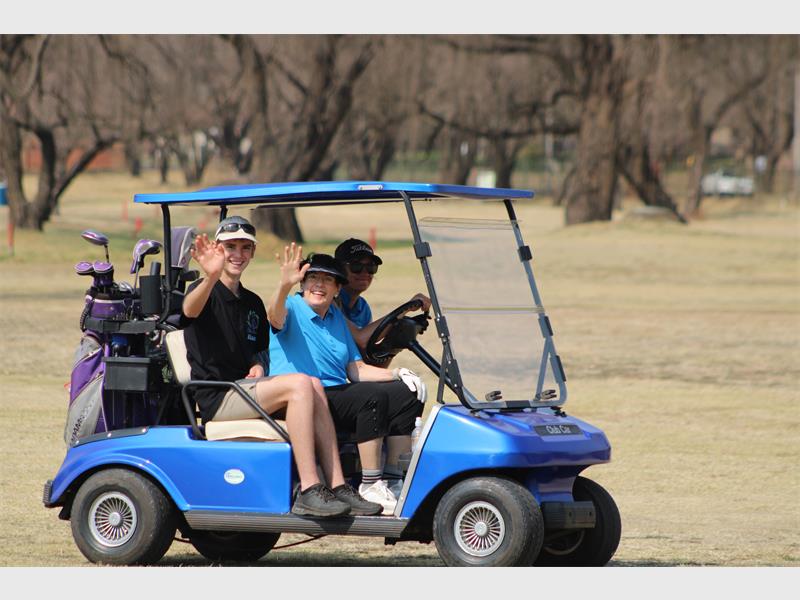 A man and woman in a golf cart waving to the camera.