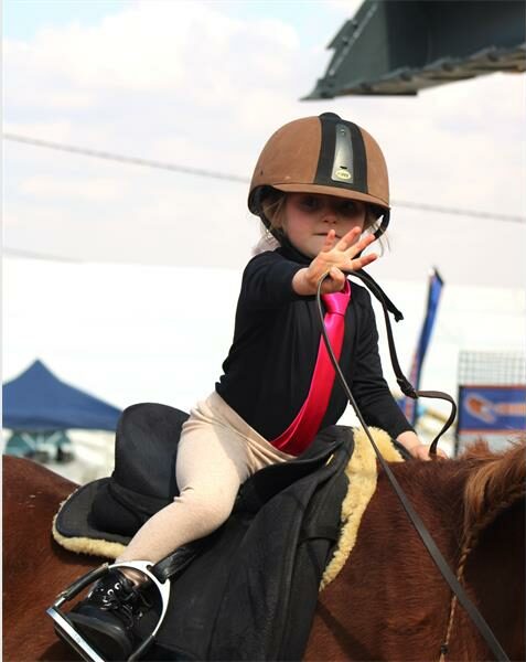 A young girl in a black and pink outfit riding a horse.