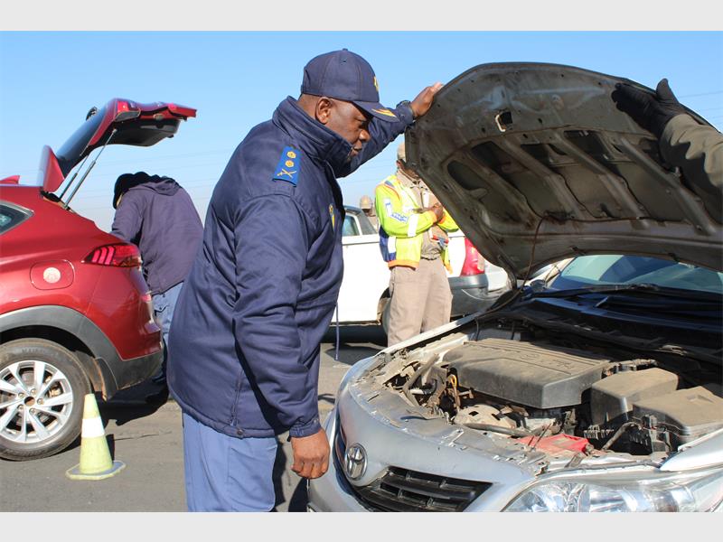 A man in a blue jacket is looking under the hood of a car.