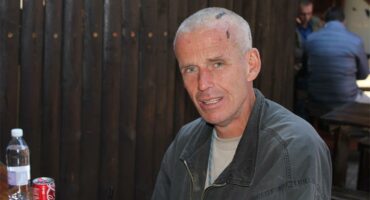 A man sitting at a table with a drink and a can of soda.