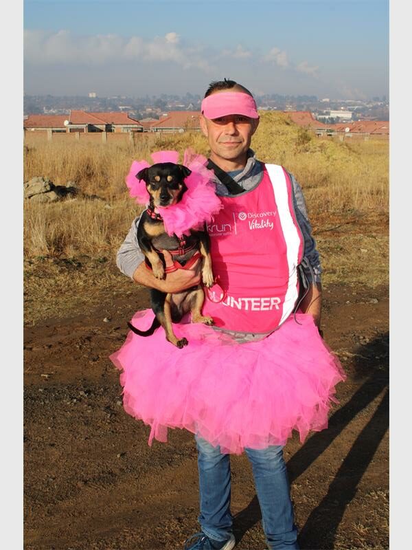 A man in pink tutu holding a dog in a pink tutu.